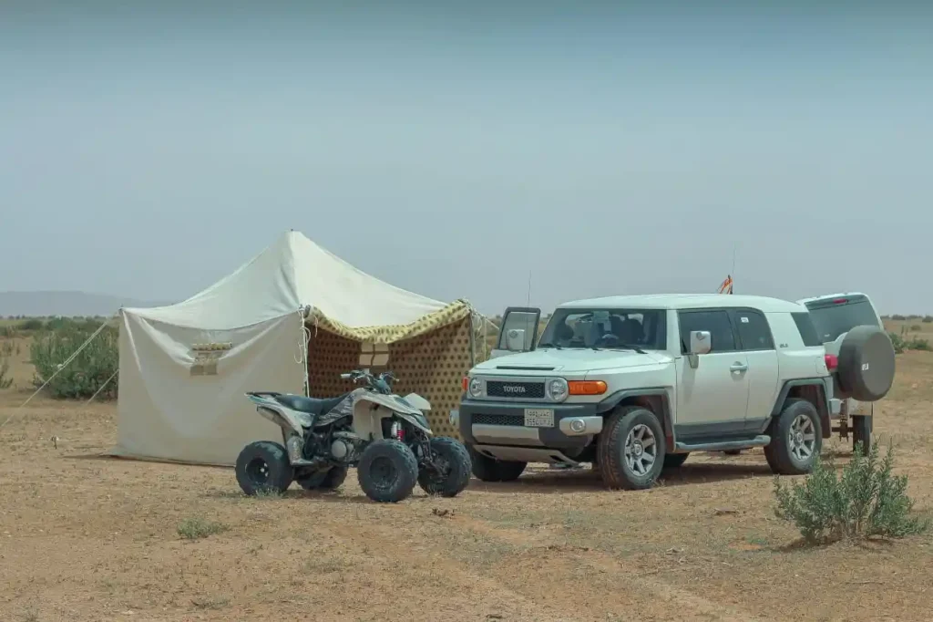 SUV and quad bike parked next to a desert tent.